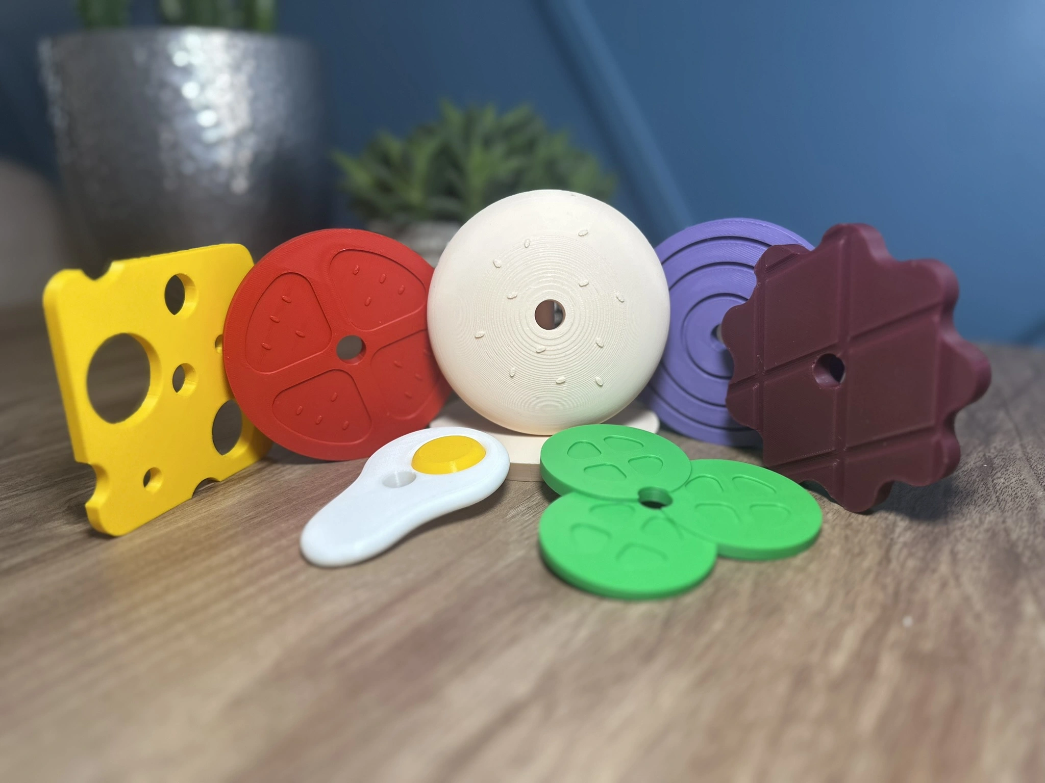 Montessori hamburger sıralama oyunu parçaları detaylı şekilde renkli olarak sergileniyor; peynir, domates, yumurta, köfte, salatalık ve ekmek katmanları 3D baskı olarak üretilmiş.